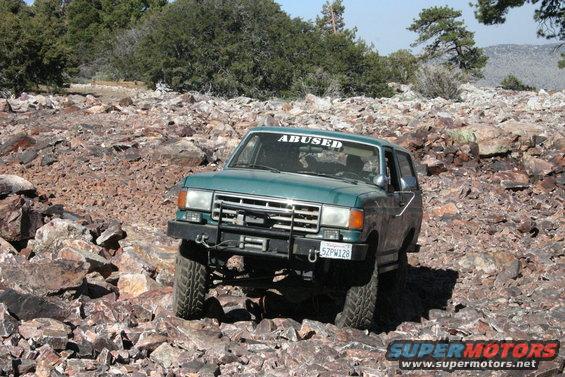 Green Ford Bronco off-roading on a rocky trail, front grille and bumper visible