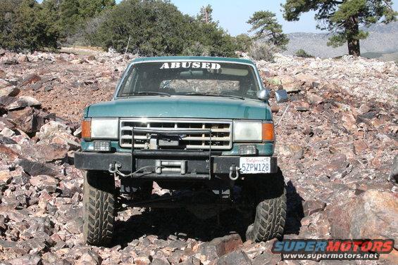 Green SUV with 'ABUSED' sticker on windshield, driving over rocks. License plate 5ZPW128