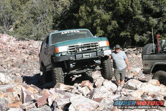 Green Ford Bronco with "ABUSED" sticker on windshield, navigating rocky terrain
