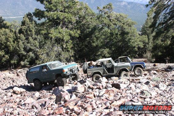 Three SUVs are driving on a rocky mountain trail. One is green, and two are gray/blue