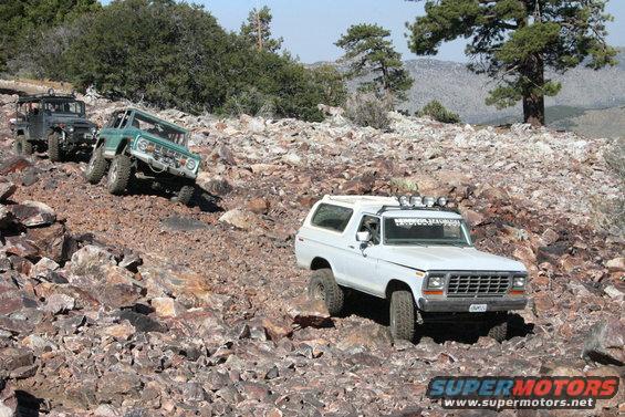 White Ford Bronco driving on a rocky trail, with two other off-road vehicles behind it