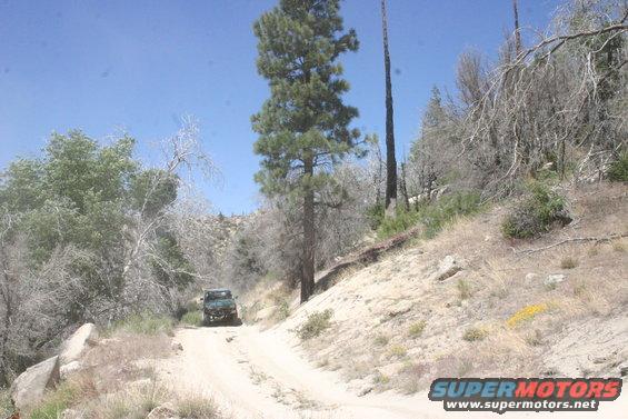 Dark green SUV on dirt road, wooded hills
