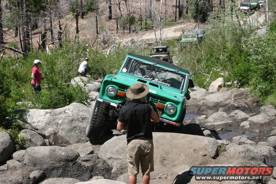 Green Ford Bronco navigating rocky terrain, "So Cal Broncos" sticker on windshield