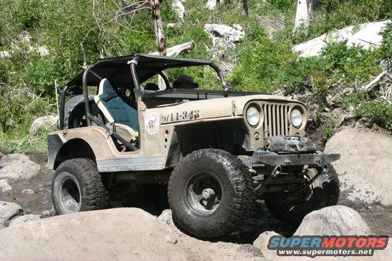 Tan Jeep CJ-7 off-roading on rocks, with a roll cage and winch