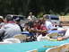 1986 Ford Bronco - A group of people are seated at tables outdoors, with several vehicles visible in the background.