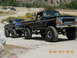 1986 Ford Bronco - Two lifted Ford pickup trucks are seen on a dirt road, with the black truck in the foreground.