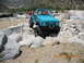 1986 Ford Bronco - A teal Suzuki Samurai navigates a rocky obstacle course with other vehicles in the background.