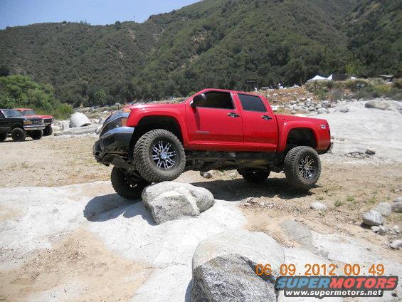 Red pickup truck with custom wheels navigating rocky terrain