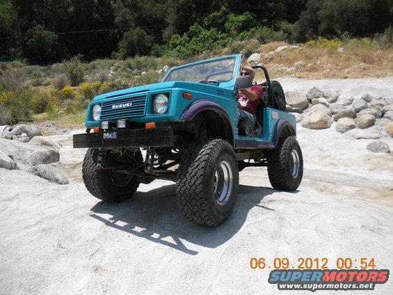 Teal Suzuki Samurai with purple fender flares and aftermarket bumper on rocky terrain