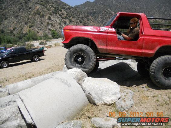 Red off-road truck with big tires navigating rocks. Black pickup truck in background