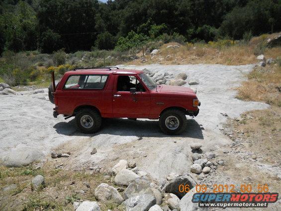 Red 1986 Ford Bronco driving on rocky terrain