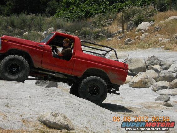 Red off-road SUV with a roll cage driving over rocks