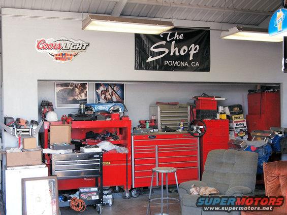 Garage interior with tool chests, a dog sleeping in a chair, and a banner reading "The Shop Pomona, CA"