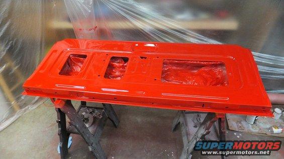 Red tailgate being painted, resting on sawhorses. Supermotors.net logo visible