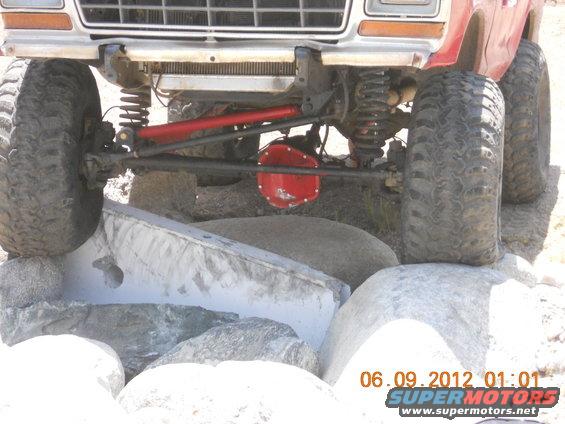 Front end of a lifted truck with large tires, navigating over rocks. Red differential visible