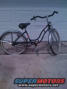 Black cruiser bicycle with whitewall tires and chrome fenders parked in front of a garage door