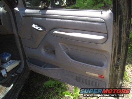 Interior door panel of a vehicle, showing gray plastic trim, window controls, and storage pockets