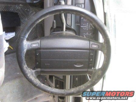 Interior shot of a vehicle's steering wheel and dashboard. The steering wheel has buttons on it