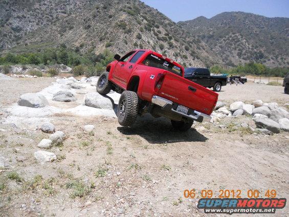 Red pickup truck navigating rocky terrain, rear view
