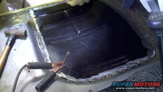 Welding a patch panel onto a car's floor pan with a hammer and welding equipment nearby