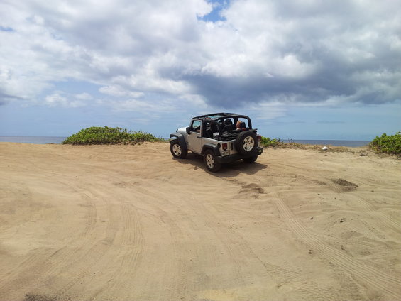 Silver Jeep Wrangler parked on sand with ocean and cloudy sky in background