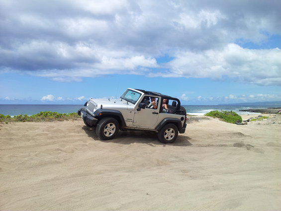 Silver Jeep Wrangler parked on a sandy dune near the ocean