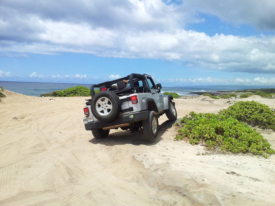 Silver Jeep Wrangler parked on a sandy beach with the ocean in the background