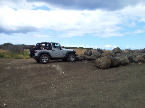 Silver Jeep Wrangler parked near a pile of large rocks under a cloudy sky