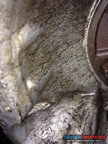 Close-up of a dirty, possibly corroded engine block interior with textured surfaces and some oil residue