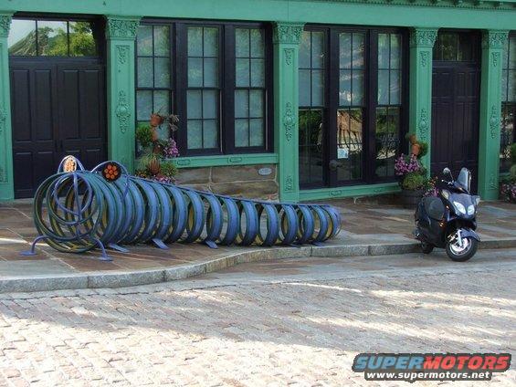 Caterpillar-shaped sculpture and a dark scooter parked on a sidewalk in front of a green building