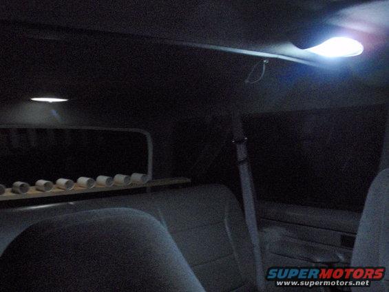 Interior view of a vehicle showing seats, overhead lights, and a shelf with cylindrical objects
