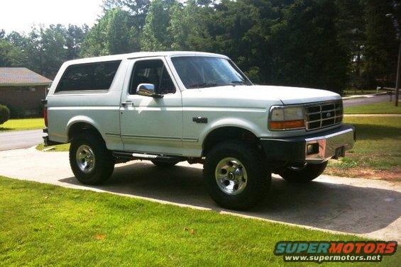 White 1993 Ford Bronco parked on a driveway with grass and trees in the background