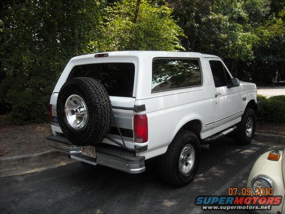 White Ford Bronco, rear 3/4 view, spare tire on back, chrome wheels, license plate visible