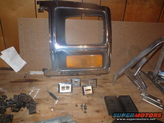 Chrome grille surround with amber turn signal and assorted small parts on a wooden surface