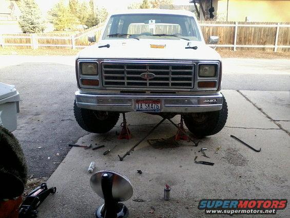 Front view of a white 1981 Ford Bronco on jack stands with tools scattered around
