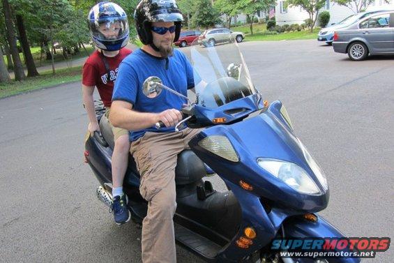 Man and child on a blue scooter, both wearing helmets