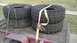 1989 Ford Bronco - Four off-road tires are strapped to a trailer, ready for transport.