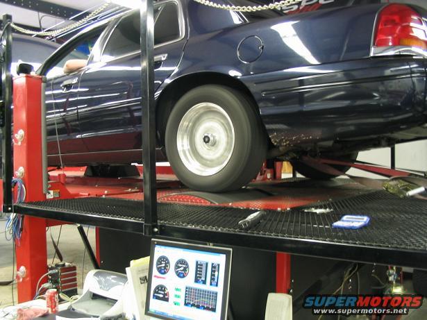 Dark blue sedan on a dynamometer, rear wheel spinning, computer monitor showing gauges
