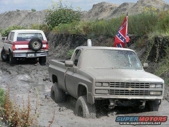 Muddy pickup truck stuck in mud with Bronco behind it. Confederate flag flying