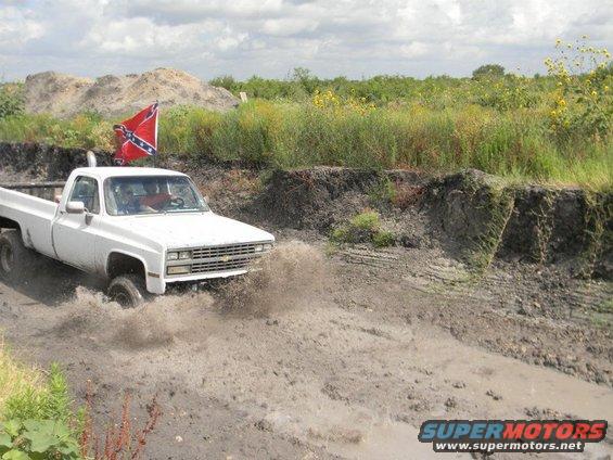 White pickup truck splashing mud, Confederate flag flying from antenna