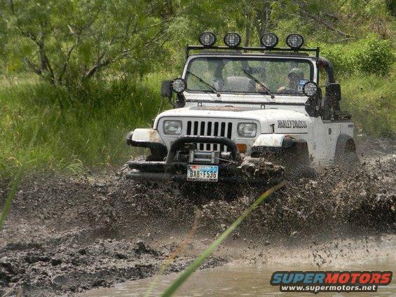 White Jeep Wrangler driving through mud, with "Harley Davidson" text on the side and a Texas license plate