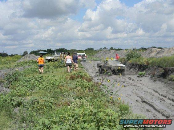 Several off-road vehicles driving through mud under a cloudy sky
