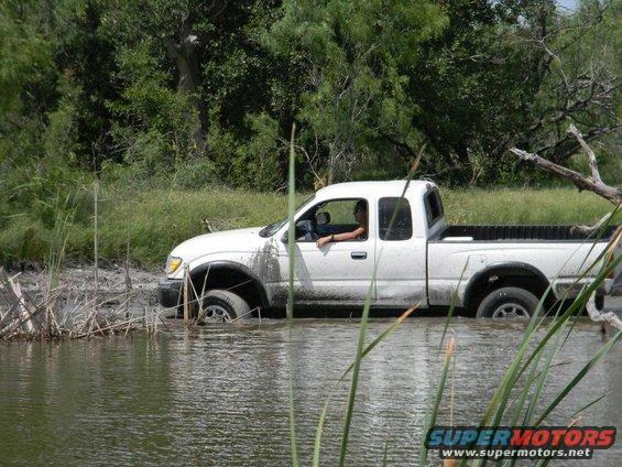 White pickup truck with driver stuck in muddy water, side view
