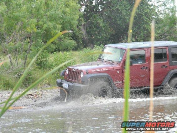 Red Jeep Wrangler Rubicon splashing through mud and water