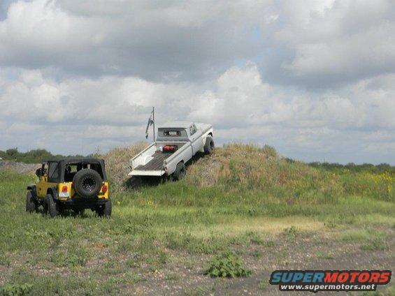 White pickup truck on a grassy hill with a yellow jeep in the foreground
