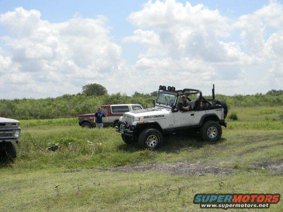 Red and white Ford Bronco parked in grassy field with a white Jeep Wrangler in the foreground