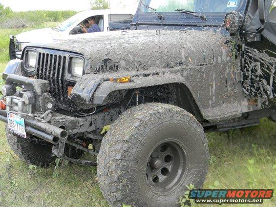 Mud-covered black Jeep Wrangler with a winch and aftermarket bumper, seen from a 3/4 front angle