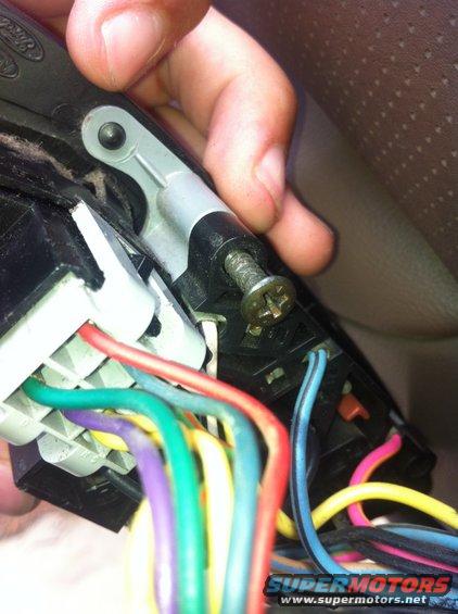 Close-up of a car's door wiring harness with multiple colored wires connected to a black plastic housing, held by a hand