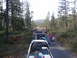 1994 Ford Bronco - A group of off-road vehicles travels down a wooded dirt road, carrying camping gear and displaying American flags.