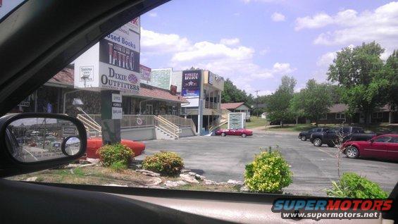 Red sedan parked in a lot with businesses in the background